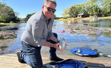 City of Palmerston Councillor Damian Hale holding a Barramundi next to a lake in Palmerston, Durack 2025.