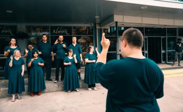 Members of an all-abilities choir singing together with their choir leader during a community performance.