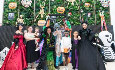 Community members and performers in Halloween costumes posing in front of a spooky Halloween display.