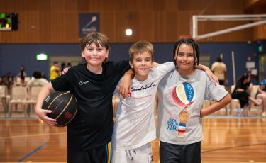 Image: 3 males smiling holding a basketball 
