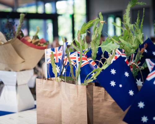 Small Australian flags sitting inside paper bags with small plants which are gifts for the new Australian Citizens