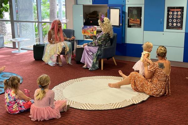 Two people reading a book with 2 children and an adult and baby