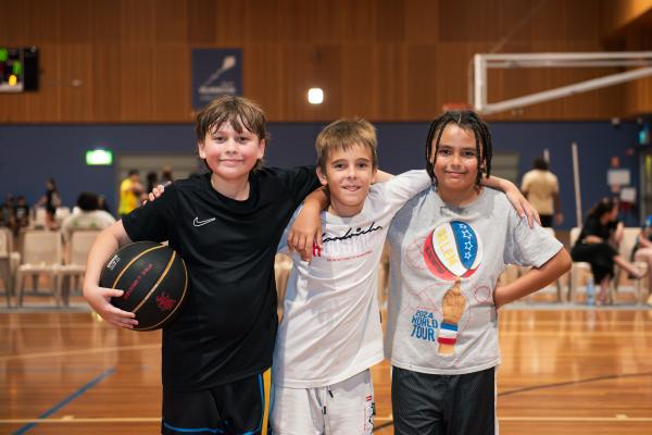 Image: 3 males smiling holding a basketball 