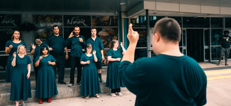 Members of an all-abilities choir singing together with their choir leader during a community performance.
