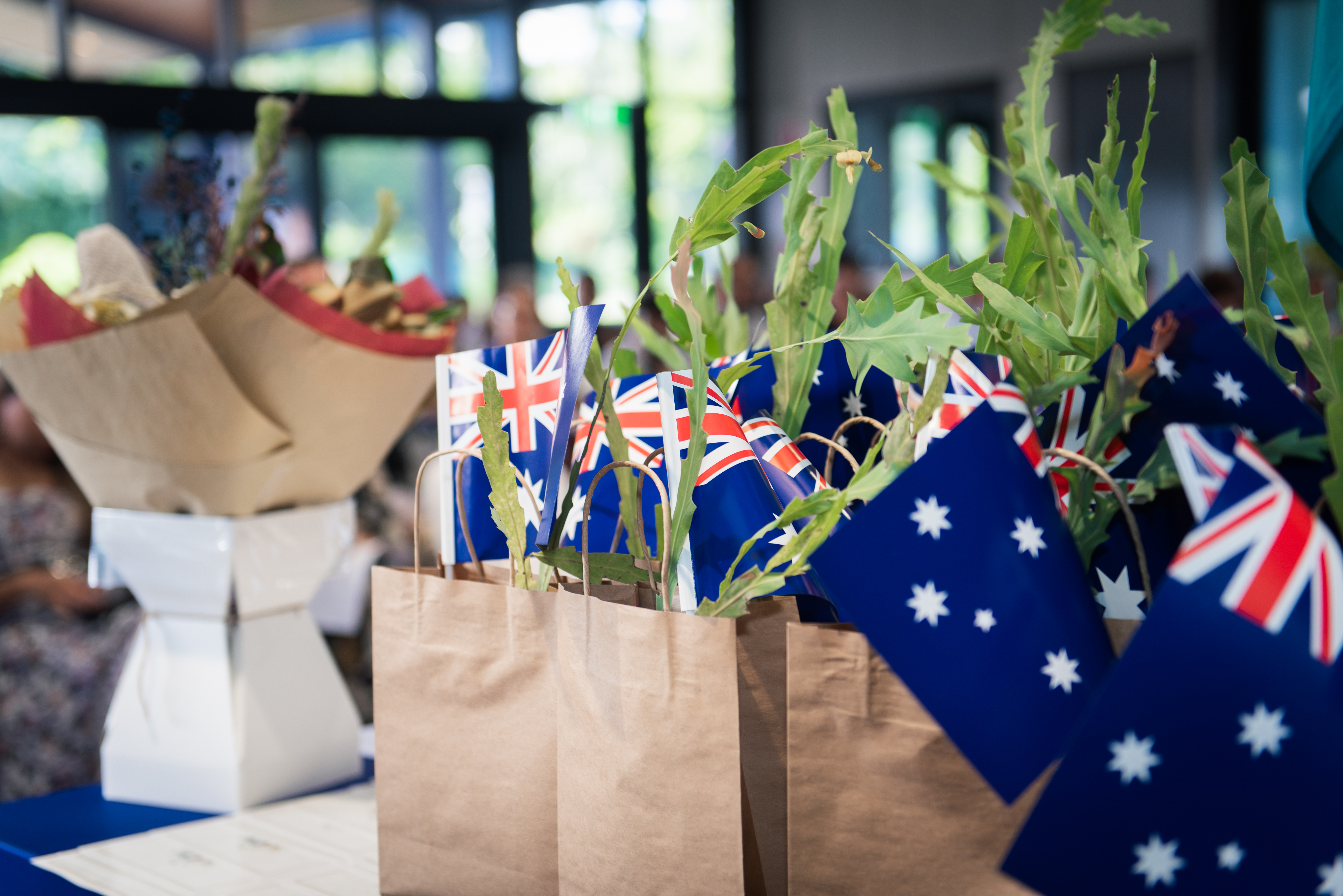 Small Australian flags sitting inside paper bags with small plants which are gifts for the new Australian Citizens